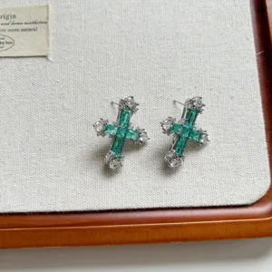 Detailed view of emerald cubic zirconia cross earrings, delicate baguette green stones.