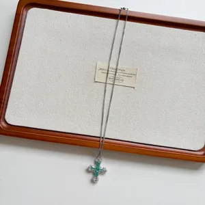 Close-up detail of silver chain necklace with green zircon cross pendant and sparkling stones.