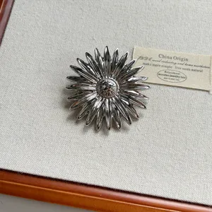 Silver metallic sunflower brooch detail shot, vintage chic design, statement jewelry accessory.