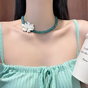 Dettaglio in primo piano della collana di perle verdi con ciondolo floreale argento.