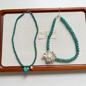 Vista dettagliata di collana di perle verdi vintage con fiore d'argento e cuore blu, piatto.