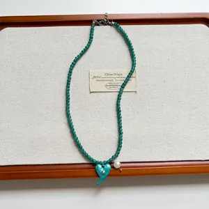 Primo piano dettagliato di collana di perle verdi retro con ciondolo cuore blu e perla.