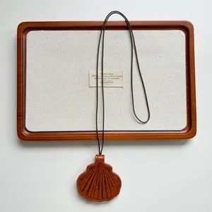 Close-up detail van de bruine lederen schelp brilhouder hanger op een minimalistisch houten dienblad.