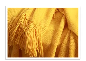 Close-up detail of soft yellow knitted throw blanket with elegant fringe and cozy texture.
