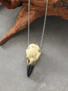 Primo piano dettagliato di collana con ciondolo teschio corvo resina su sfondo grigio.