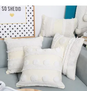 Detail view of boho tufted throw pillow with pom pom fringe on neutral beige cotton fabric.