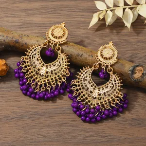 Close-up of bohemian hollow gold earrings with purple beaded fringe on a rustic wooden background.