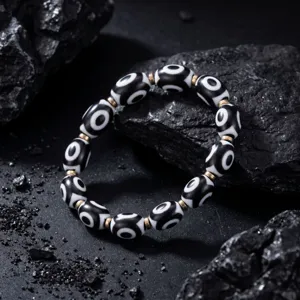 Detail shot of Tibetan black and white Dzi bead bracelet with metal spacers on dark rock surface.