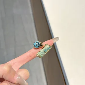 Detail shot of a vintage style metal ring featuring a blue ladybug and green stone geometric decor.