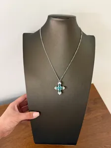 Vista dettagliata di una collana con ciondolo a croce argento con cristallo blu-verde.