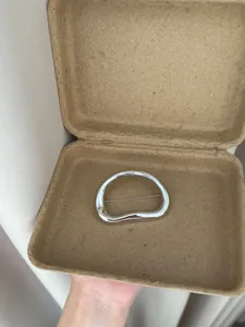 Close-up view of the minimalist irregular metal brooch displayed inside a natural box.