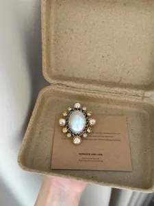 Vintage pearl rhinestone metal brooch detail shot, elegant accessory in kraft gift box.