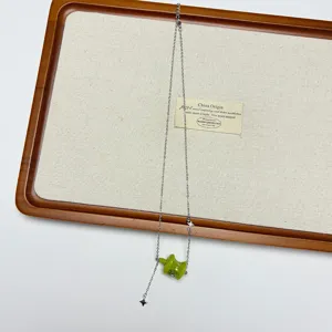 Delicate green apple pendant necklace detail, silver chain with elegant tassel and star design.