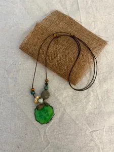 Detail shot of boho green resin fruit slice necklace with wooden beads and long braided cord.
