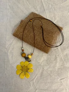 Detail shot of the resin yellow flower pendant necklace featuring wooden beads and long cord.