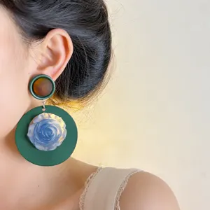 Close-up of vintage green wooden geometric earrings featuring a unique blue flower detail.