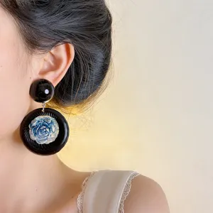 Close-up detail view of vintage black statement earrings with a blue flower pendant for women.