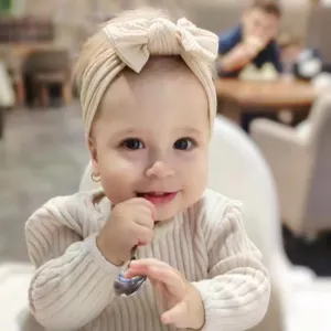Bebé adorable con una suave diadema de nailon beige con lazo en un entorno cotidiano