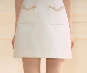 Elegant white mini skirt with stylish front pockets and delicate pearl trim detailing.