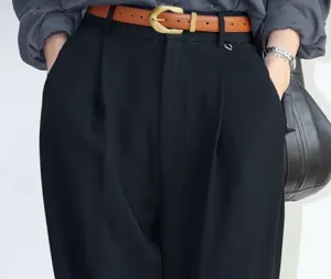 Close-up detail of a brown leather belt with brass buckle worn with black trousers.