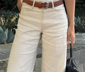 Detail shot of a stylish brown braided belt with a silver pin buckle worn on casual white pants.