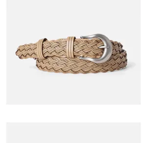 Close-up detail of a classic khaki braided leather belt with silver pin buckle for women.