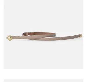 Detailed shot of a sleek taupe leather belt featuring elegant gold-tone spherical ends.