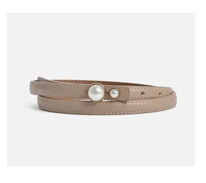 Close-up detail of women's thin beige leather belt with elegant pearl decorative buckle.