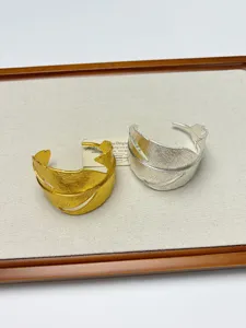 Close-up detail of metal leaf open cuffs in gold and silver colors, elegant jewelry display.