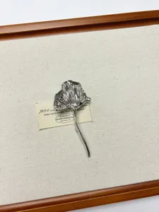 Close up detail of silver metallic pleated leaf brooch, vintage style clothing accessory.