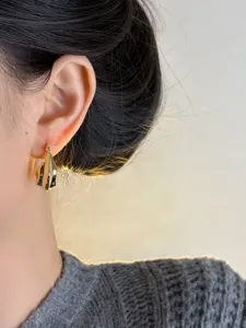 Close-up detail of trendy irregular folded gold metal hoop earrings, elegant minimalist jewelry.