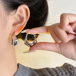 Silver metal geometric earrings featuring unique irregular design, shown worn on ear and hand.