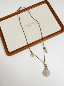 Detail shot of bohemian ocean style seashell necklace with adjustable leather cord on wooden tray.