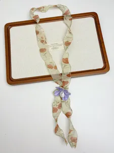 Close-up detail of vintage floral silk scarf necklace with purple flower and white bead accent.