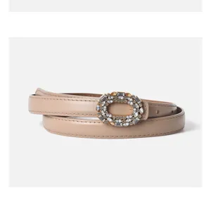 Close-up detail of the beige leather belt featuring a sparkling oval rhinestone buckle.