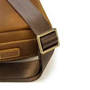 Gros plan sur la sangle et la bouclerie vintage d'un sac bandoulière en cuir pour homme.