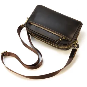 Vue detaillee d'un sac bandouliere en cuir marron vintage avec fermetures eclair et sangle.