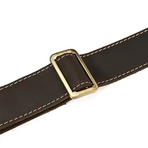 Close-up detail shot of genuine leather vintage travel bag strap featuring a bronze metal buckle.