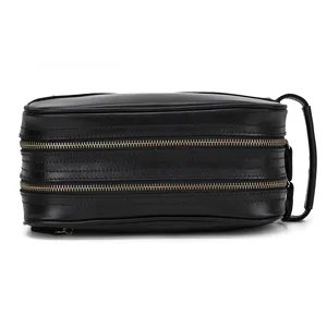 Close-up detail of the black leather toiletry bag showing double zippers and side handle.