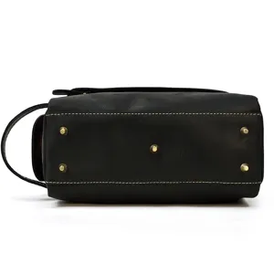 Close-up detail view of black leather toiletry bag bottom with metal feet and fine stitching.