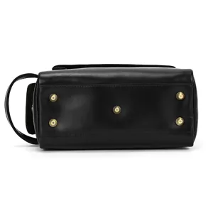 Black leather toiletry bag bottom detail showing sturdy brass feet and convenient side handle.