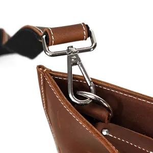 Gros plan detail de sac bandouliere en cuir vintage avec mousqueton et coutures.