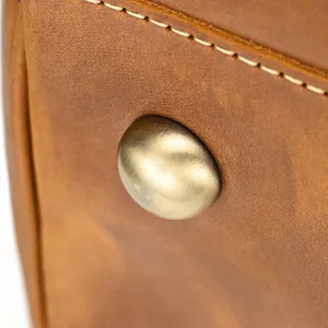 Close-up detail of genuine leather travel bag with vintage metallic bottom stud and stitching.