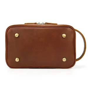 Detailed view of the brown leather toiletry bag bottom with protective metal feet and strap.