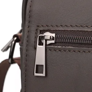 Detalle de cremallera de bolso de cuero marrón para hombre con costuras finas y textura.