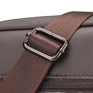 Primer plano de la hebilla de ajuste y correa metálica de un bolso de cuero para hombre.