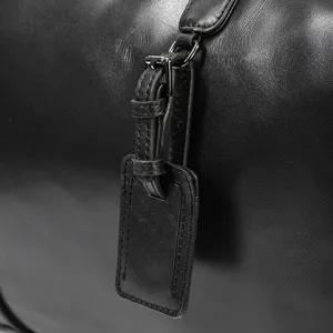 Detailed view of black leather travel bag strap and metal hardware texture craftsmanship.