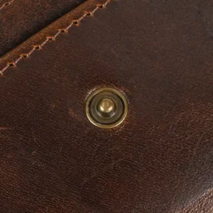 Close-up detail of retro leather wallet showing vintage brass snap button and fine stitching texture.