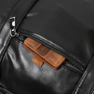 Close up detail of black leather travel duffel bag zipper pocket and brown leather accent.