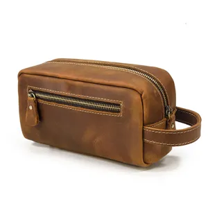 Brown leather toiletry bag detail showing vintage texture, smooth metal zipper and side handle.